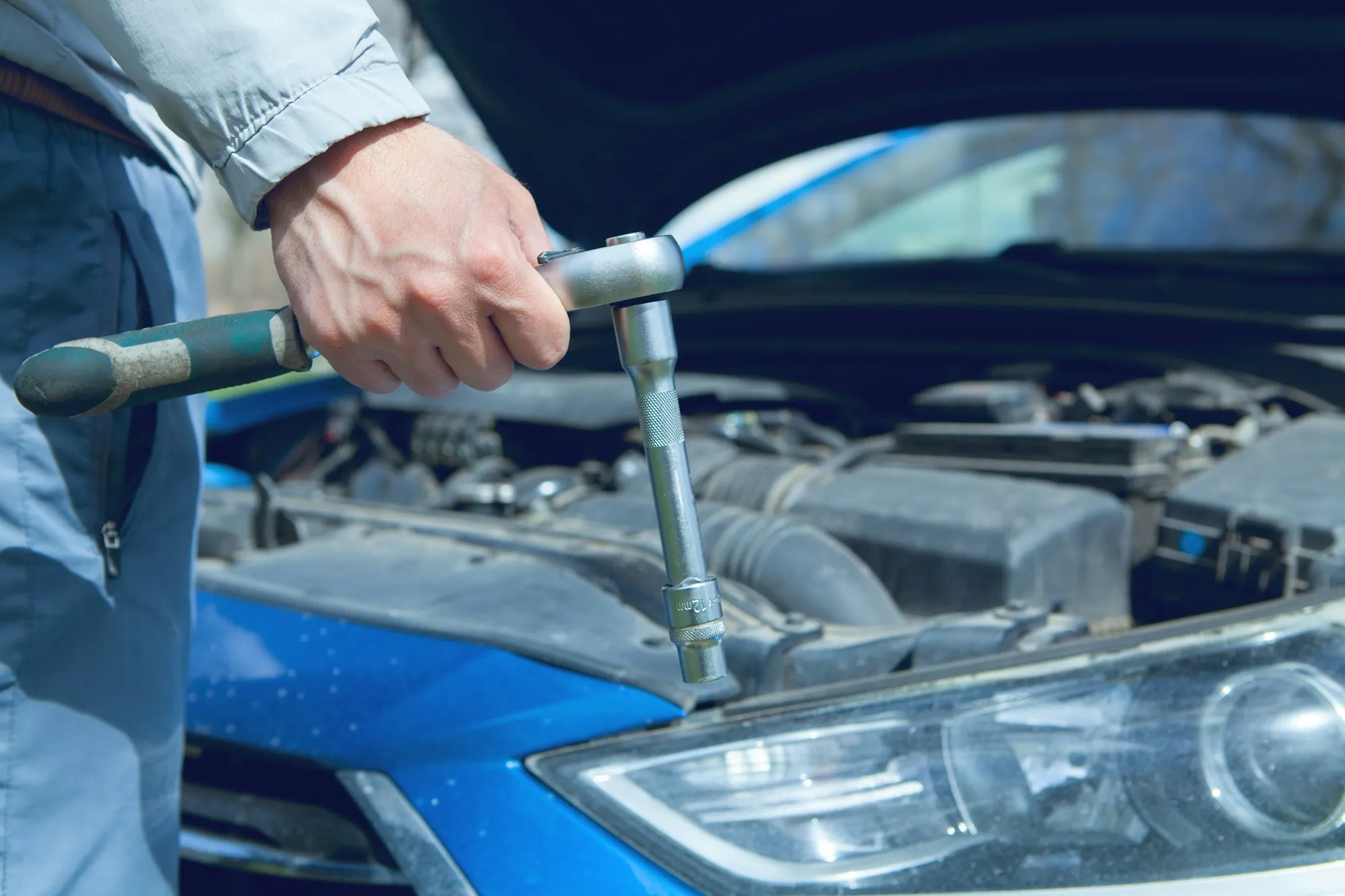 Hands turning a ratchet on an engine under an open hood