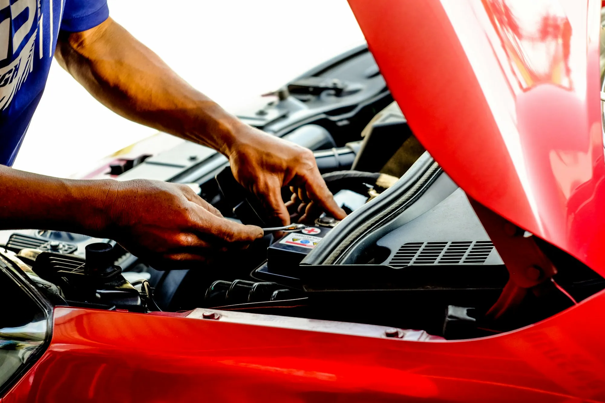 Mechanic's hands working inside a red car's engine bay