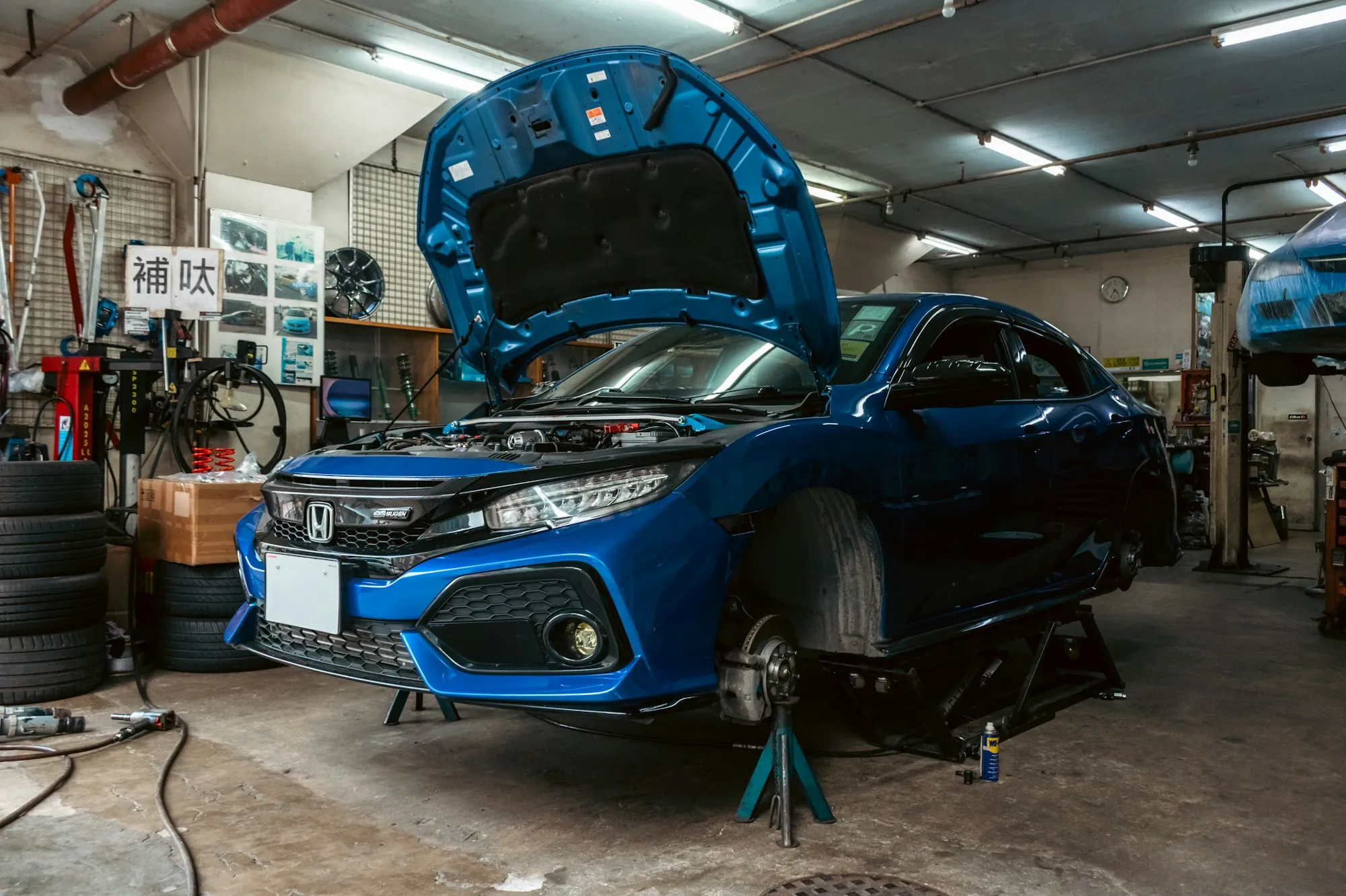 Blue hatchback raised on a shop lift with the hood open for inspection